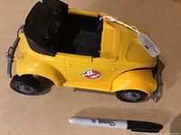 Top and side view of the vintage yellow Ghostbusters buggy toy vehicle showing the logo on the door and black interior seating.