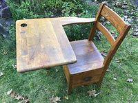 Side view of solid oak child's school desk on grass showing attached chair, writing surface with ink well hole and pen groove and bottom storage drawer