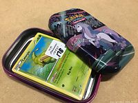 Metal tin partially open showing the top few Pokemon cards including a Caterpie card.