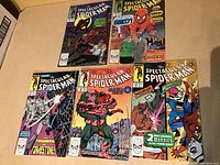 Five The Spectacular Spider-Man comic books laid out on a beige surface, showing full cover artwork and titles, highlighting the variety within the lot.