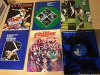 Photo showing six baseball team yearbooks from the 1970s, featuring Detroit Tigers, Kansas City Royals, and Philadelphia Phillies with various illustrated and photographic covers.