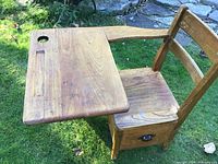 View of antique child's oak school desk showing attached seat, angled writing surface with inkwell hole, and side profile.