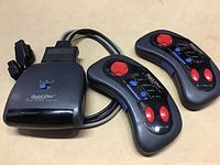 Photo showing three QuickShot controllers and one adapter unit, cables attached, all black with red and blue control buttons.