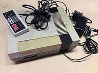 Nintendo Entertainment System console with controller and power adapter on beige surface.