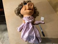 Full view of the Miss Piggy puppet lying on a flat surface, showing the entire figure with dress and gloves.