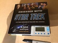 Star Trek Obsessed With trivia book with handheld game device and a Sharpie marker on a flat surface.