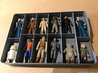 Top-down view of 14 Star Wars original trilogy Kenner figures organized in a tray with 12 compartments, showing full figures and detail of colors and wear.