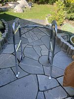 Front and side view of the walker standing on a stone patio, showing metal frame with two wheels on front and rubber tips on rear legs.