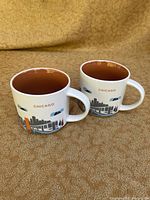 Pair of large Starbucks Chicago ceramic mugs shown from a side angle illustrating skyline, train, and Chicago label with brown glazed interior