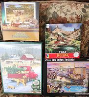 Photo showing all four jigsaw puzzle boxes arranged: Wilderness Animal Library by Bo Newell 1000 pieces, Blaylock steam train 750 pieces, Cobble Hill Vermont snowy scene with red truck 1000 pieces, and Las Vegas Twilight 1000 pieces.