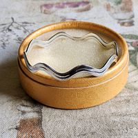 Sterling silver wavy bangle displayed in round golden box with foam insert
