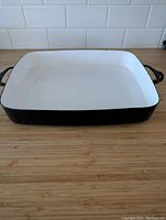 Full view of rectangular black enamel pan with white interior on wood surface, showing both handles.