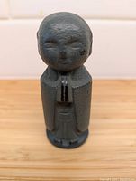 Front view of dark green stone Buddha statuette showing folded hands and smooth rounded head with closed eyes.