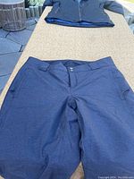 Blue-gray snowboarding pants laid flat showing front with zippered pockets and button closure.