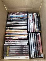 Photo showing a large assortment of DVDs stacked inside a cardboard box. Titles visible include The Hours, The Dark Purple, Miss Potter and others.