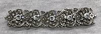 Close-up photo of a decorative bracelet showing detailed, vintage style metalwork and multiple clear crystals inlaid in the design.