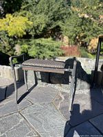 Vintage garden kneeler bench shown in upright position, metal frame with padded woven seat and handle supports.