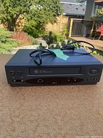 Front angled view of a black GE VHS player showing the cassette loading door, top surface, and power cable.