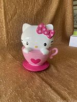 Front view of the Hello Kitty ceramic coin bank with pink teacup and bow detail.