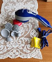 Blue and gray handheld electric Homedics massager with red heating massage head and six gray interchangeable attachments on a lace cloth.
