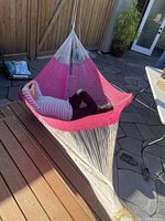 View of large pink and white woven hammock outdoors with a person lying inside to demonstrate size and comfort. Visible are attached ropes and hanging loops at the ends.
