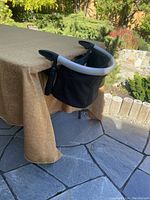 Child seat clamped to table edge with silver metal clamp frame and black fabric seat with straps