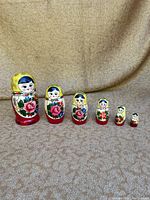 Full set of 6 colorful Matryoshka dolls arranged from largest to smallest on beige fabric
