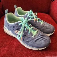 Side view of new purple Skechers running shoes with aqua green laces on a red surface.