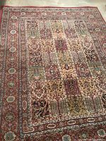 Photo shows a vintage Persian style carpet with intricate patchwork motif mainly in reds, creams, greens, and browns; bordered with floral and geometric patterns.