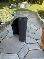 Carpet runner rolled standing on a flagstone surface outdoors, showing thickness and rubber backing.