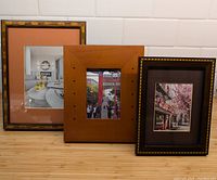 Three wooden picture frames of different sizes and colors arranged on counter under tiles, featuring different styled photos inside.