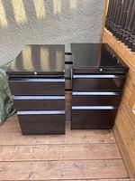 Pair of black metal file cabinets side by side showing overall condition and design, two drawers each with locks on top drawers.