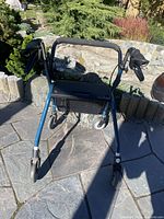 Front view of blue metal walker with four wheels, seat area, hand grips, and removable basket.