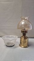Full view of brass oil lamp and separate glass lamp shade together on display surface.