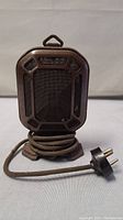 Front view of antique microphone showing metal frame and mesh grille, cord coiled at base with plugged end