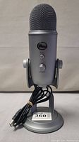 Front view of Blue Yeti USB microphone showing metal mesh top, mute button, volume knob, and attached USB cable coiled on stand.