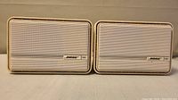 Front view of the two BOSE 151 Environmental Speakers showing the white metal grille and logo badges.