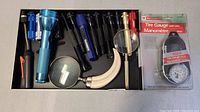 Multiple assorted flashlights, two magnifying glasses, and a new tire pressure gauge in original packaging shown in single tray
