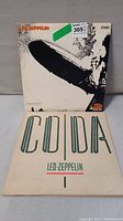 Two Led Zeppelin LP vinyl records with covers displayed, showing Led Zeppelin I with the Hindenburg disaster image and Coda album cover with text.