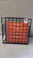 Black plastic grid record rack containing several LP vinyl records with visible orange and beige album covers.