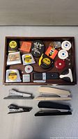 Photo showing all staplers and measuring tapes arranged on a flat surface and tray.
