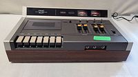 Front angled view of the TEAC A-170 stereo cassette deck showing mechanical buttons, VU meters, and wood grain side panels.