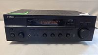 Front view of Yamaha RX-497 stereo receiver, showing brand name, model number, and digital display tuned to FM 99.9 MHz with lights on.