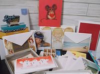 Various greeting cards laid out including Christmas snowmen, Father's Day, artistic prints, mouse heart card, and blank cards with envelopes.