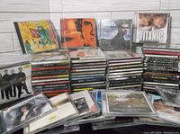 Photo showing multiple stacks of assorted music CDs in jewel cases. Visible albums include Mozart, Joe Cocker, Titanic soundtrack, and others.