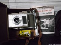 Polaroid Model J33 Electric Eye Land Camera with instruction manual and film cartridge inside an open brown case.