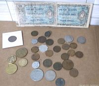 Overview of assorted foreign coins arranged on a flat surface with two German 10 Mark banknotes placed behind them.