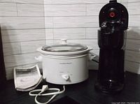 White Hamilton Beach 3 quart slow cooker with glass lid, power cord, and instruction manual on counter against a tile backsplash.