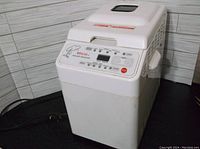 Front and top view of Regal K8771 breadmaker, showing control panel, power cord, and lid with viewing window