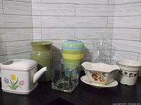 Full lot of seven vases and decorative pots displayed against a tiled wall on a black surface.